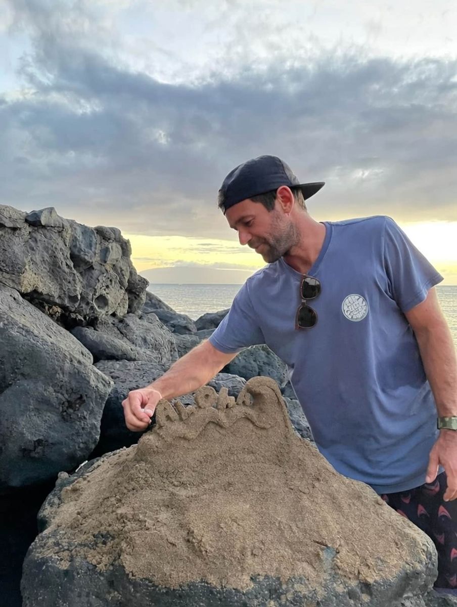 Mitchell sculpting a sand mound on the rocks at sunset
